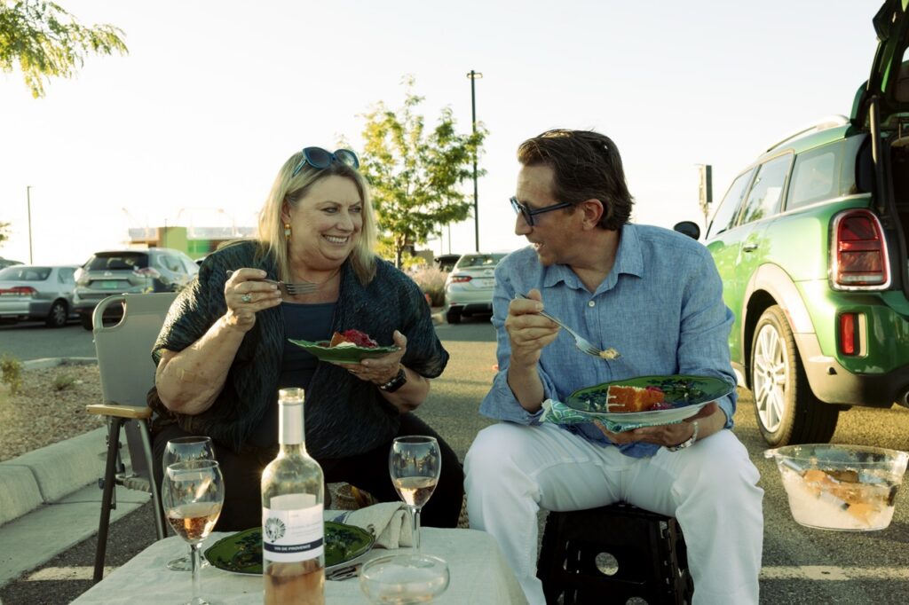 A man and a woman eat food together on a bench.