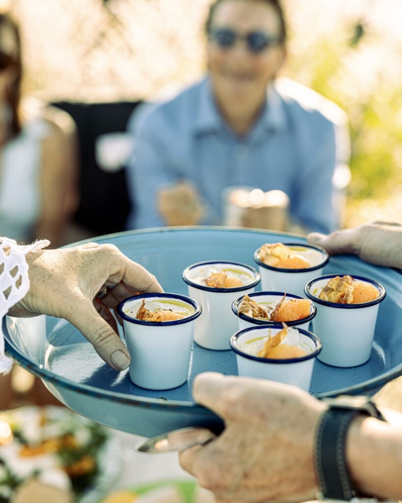 A blue plate full of small sampler cups full of food as people take them off it.