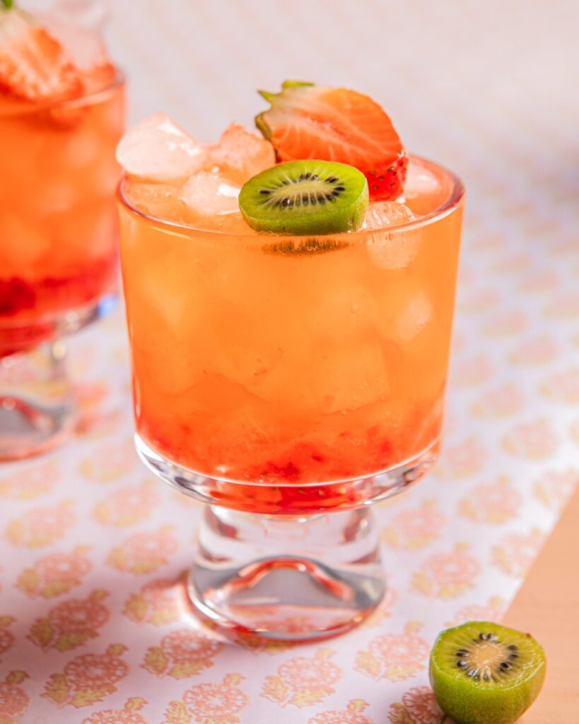 A glass full of a Strawberry Kiwi Bramble with a kiwi slice and strawberry on top.