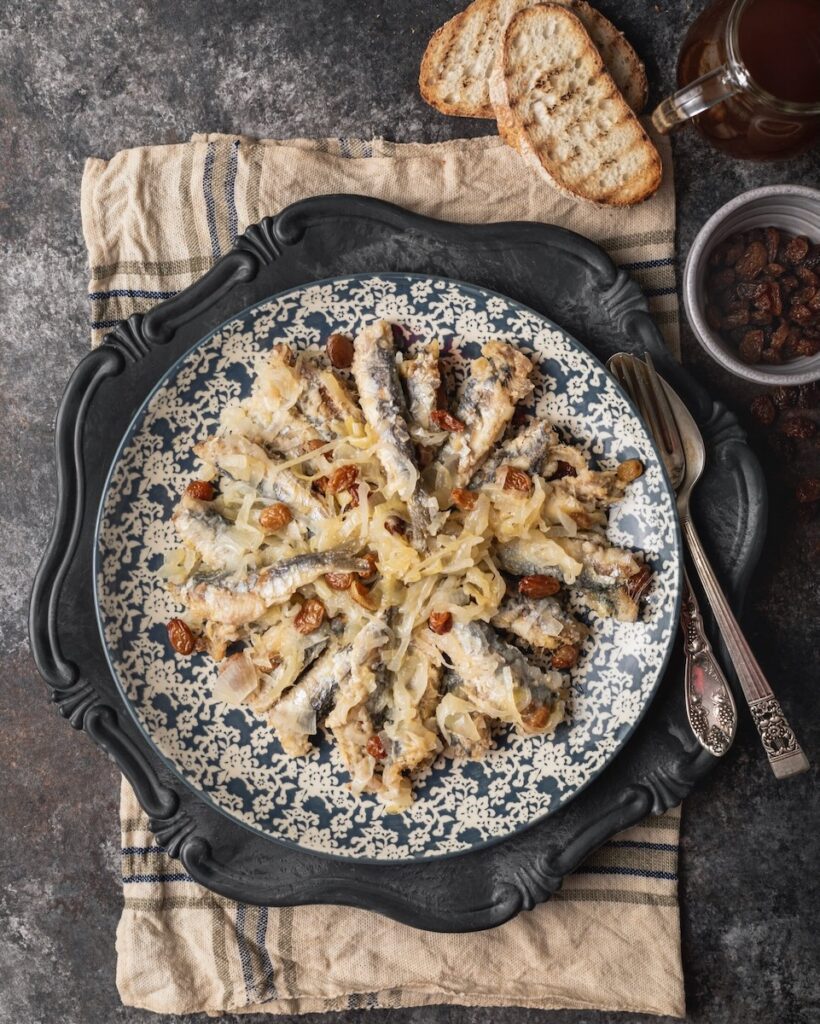 Sarde in Saor on a porcelain plate set on a rustic table.