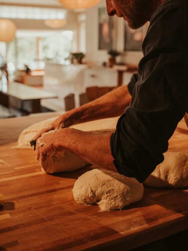 Baker hand-shaping fresh sourdough bread dough on a wooden workspace at TNT Taos.