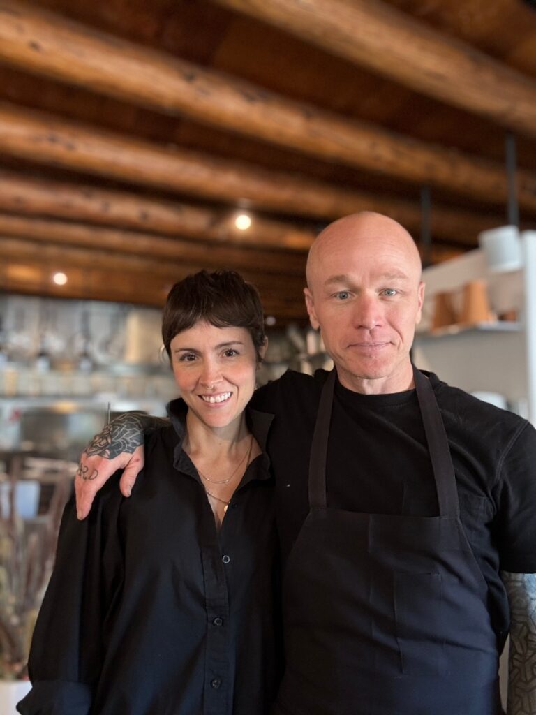 Owners Meg and Kevin Sousa standing inside Suchness dining room, featuring minimalist decor and a large blue canvas.