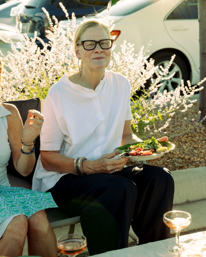 A guest in a white shirt and glasses holding a plate of gourmet appetizers at a Santa Fe Opera parking lot tailgate.