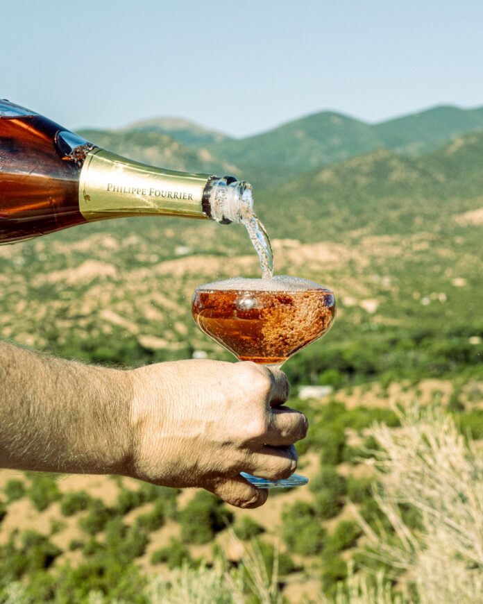 Chilled Philippe Fourrier rosé champagne being poured into a coupe glass with the Santa Fe hills in the background.