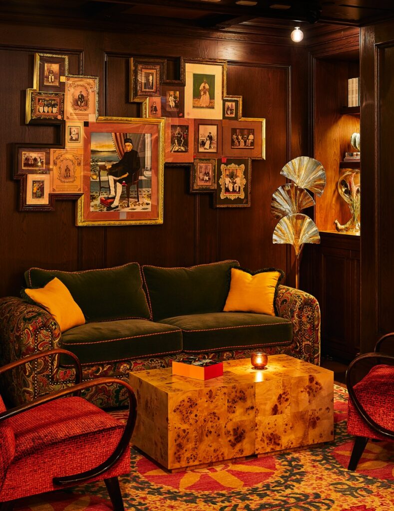 The moody and sophisticated Portrait Bar at The Fifth Avenue Hotel, featuring dark wood shelving, a large fireplace, and framed portraits.
