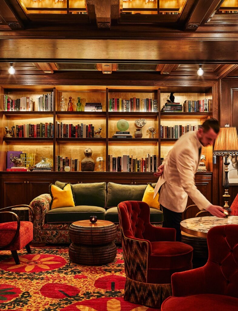 A cozy seating nook in The Portrait Bar at The Fifth Avenue Hotel with plush red velvet chairs and curated artwork.