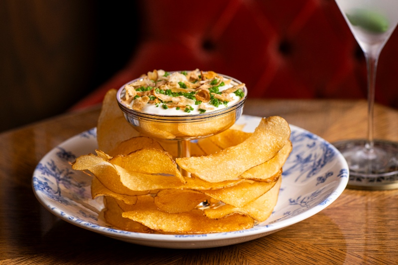 A gourmet French onion dip served with golden potato chips, an upscale bar snack at The Portrait Bar in The Fifth Avenue Hotel.