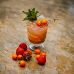 A short glass with a reddish tint and mint in the cocktail with cherry tomatoes and strawberries.
