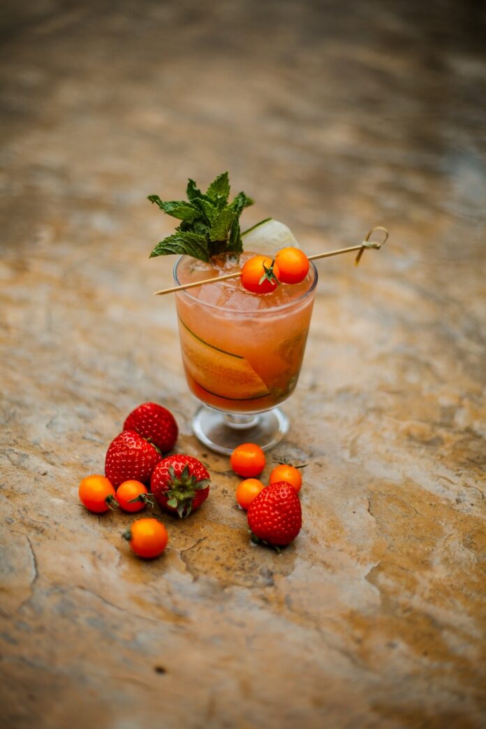 A short glass with a reddish tint and mint in the cocktail with cherry tomatoes and strawberries.