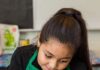 Meet Carmen Benson, Executive Director of Santa Fe’s Cooking with Kids A little girl chopping up dough on a cutting board with a green apron on.
