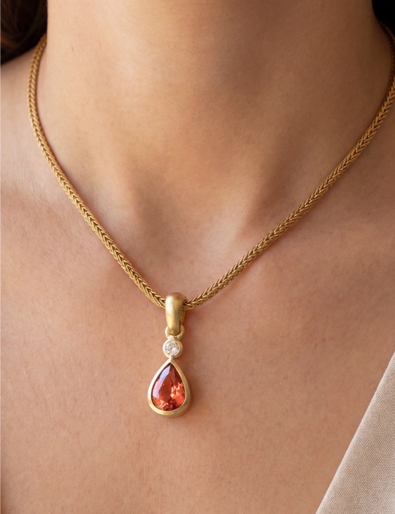An orange gem necklace sits around a woman's neck in gold.