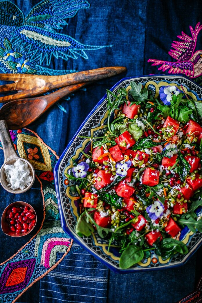 A container of salad with tomatoes on top sits on a dark blue pattern textile.