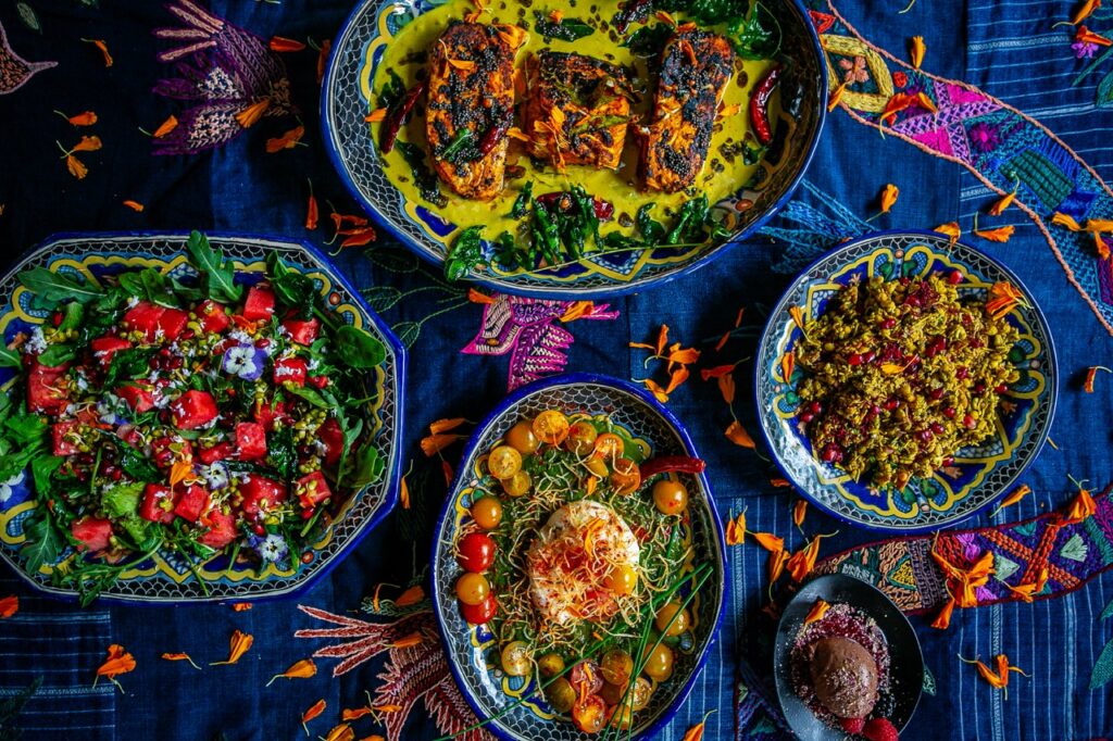 Four plates full of rice, salad, chicken, and more sit on a dark blue pattern textile.