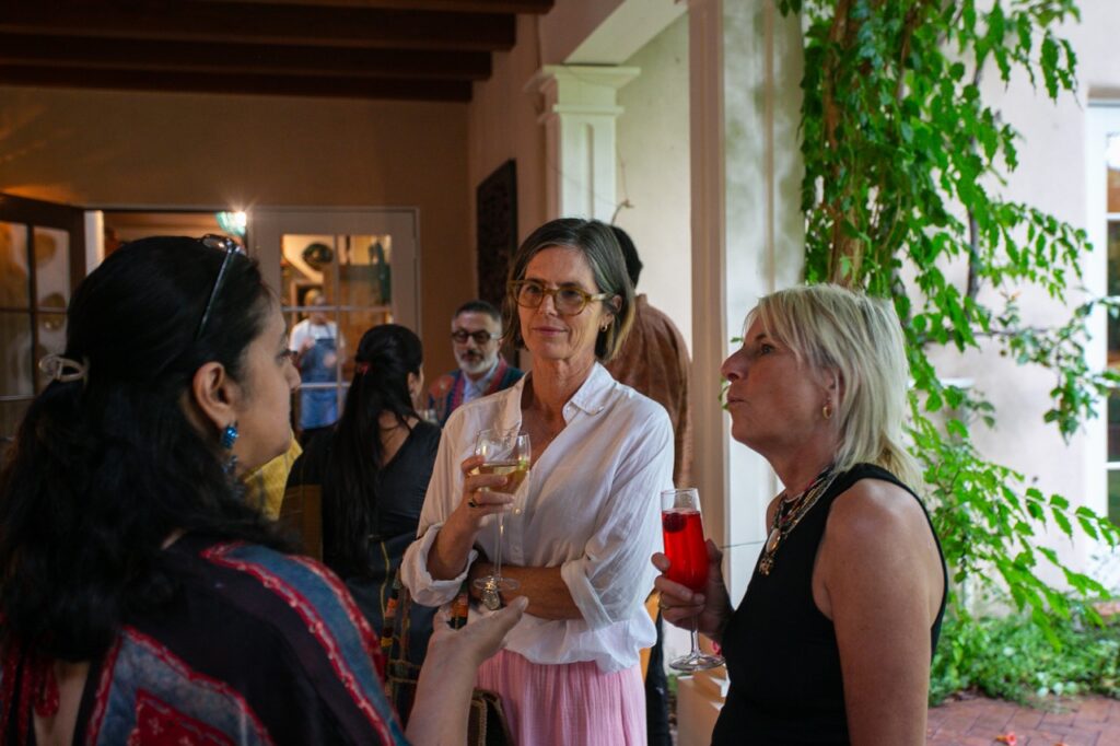 Three women talk at a party with champagne in hand.