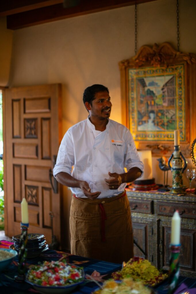 A chef in a white jacket explains the dishes on the table.