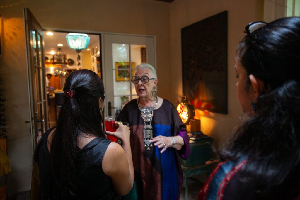 A woman in a long textile dress talks to another woman.