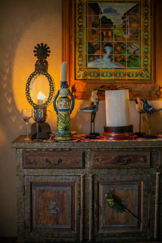 Folk art decor sits on a stand under a painting.