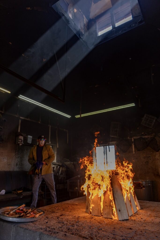 A fire burns in the center of the ceramist hut.