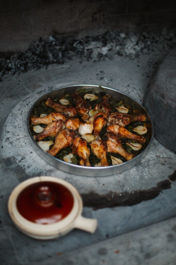 Chicken wings in a stone oven beside a sauce.