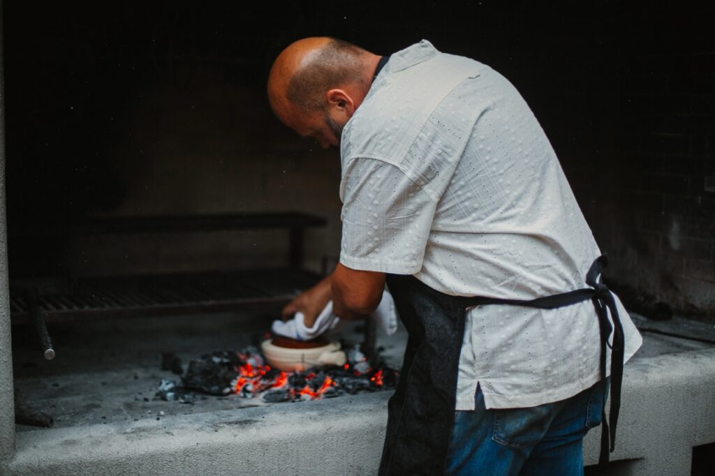 A man in an apron cleans a pot over a grill.
