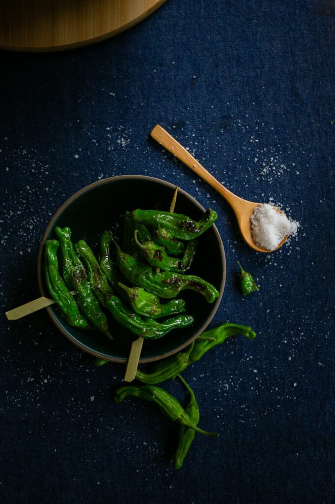 Grilled peppers on skewers inside a bowl beside a spoonful of salt.