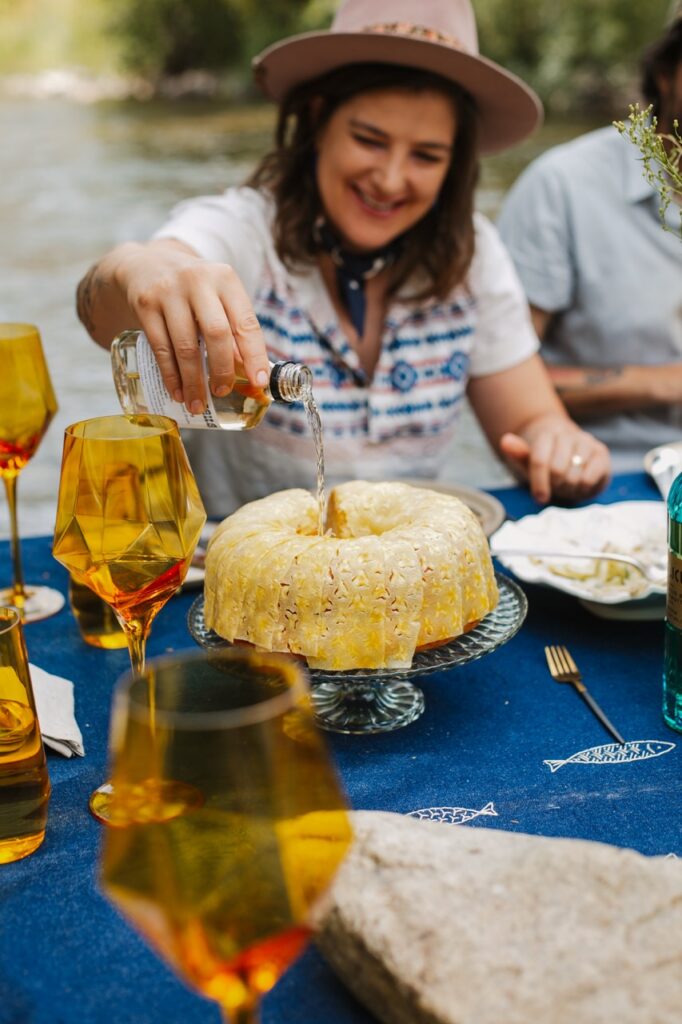 A woman in a hat pours rum into the middle of a rum cake.