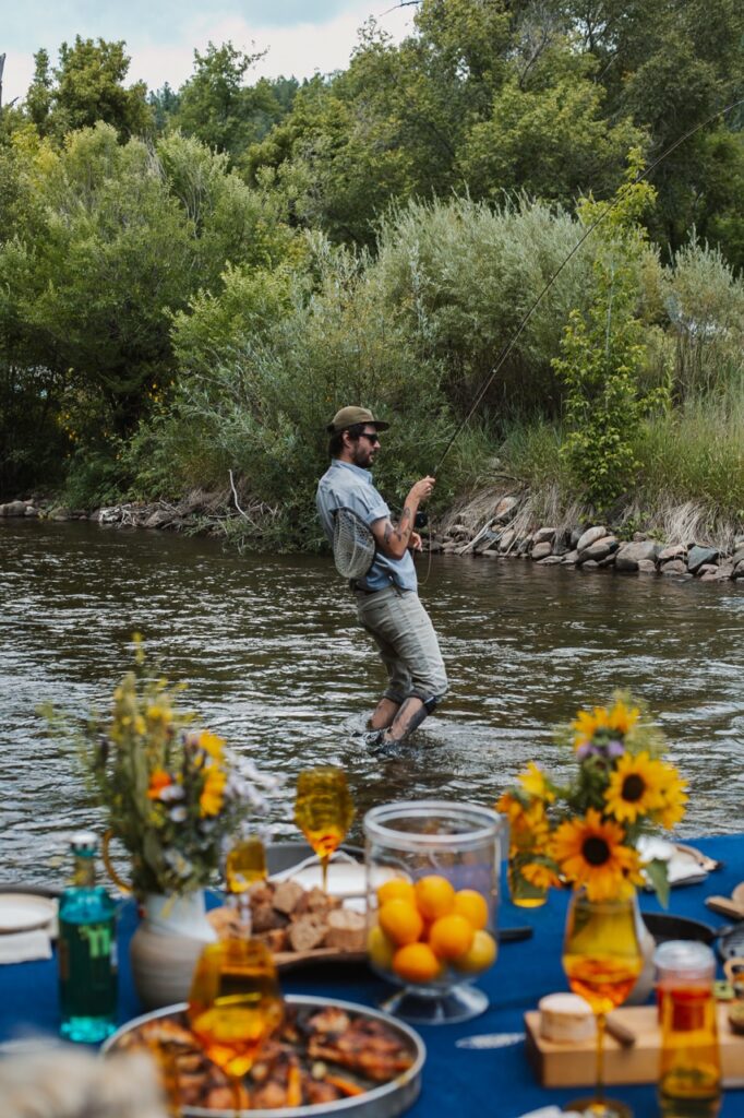 A man fishing in the river beyond a set blue table.