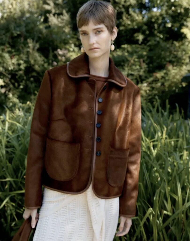 A woman in a brown zip up jacket and white skirt.