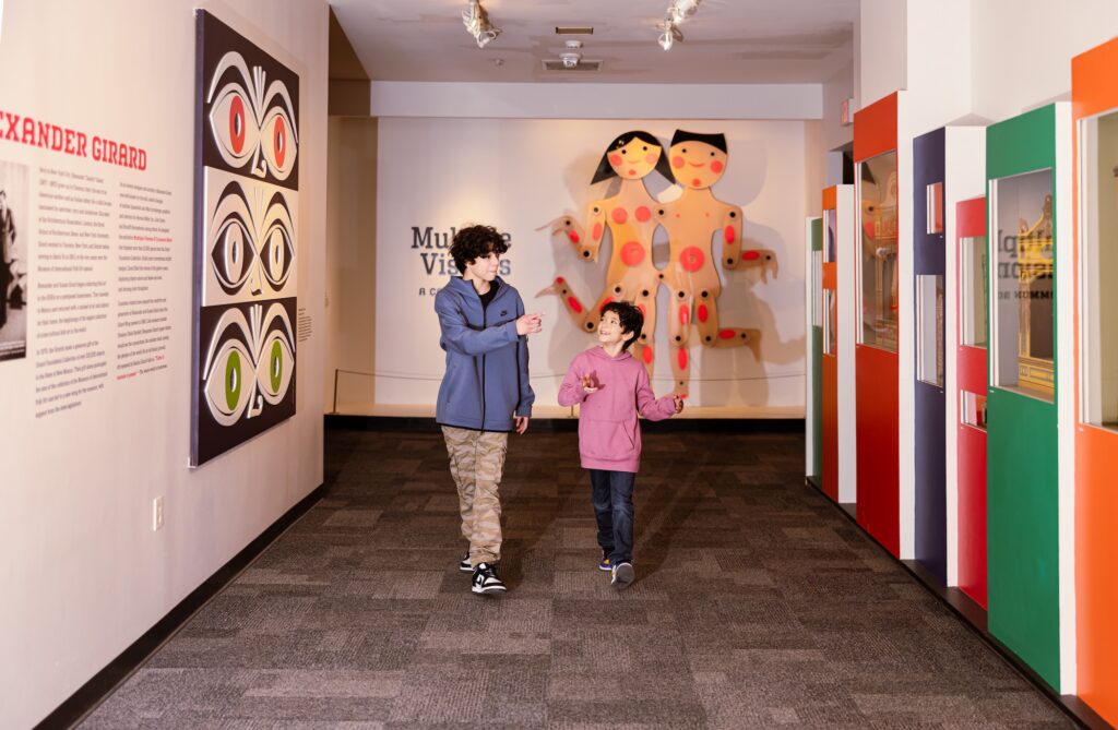Two young boys walking down a museum corridor pointing at colorful art on the walls of the Museum of International Folk Art