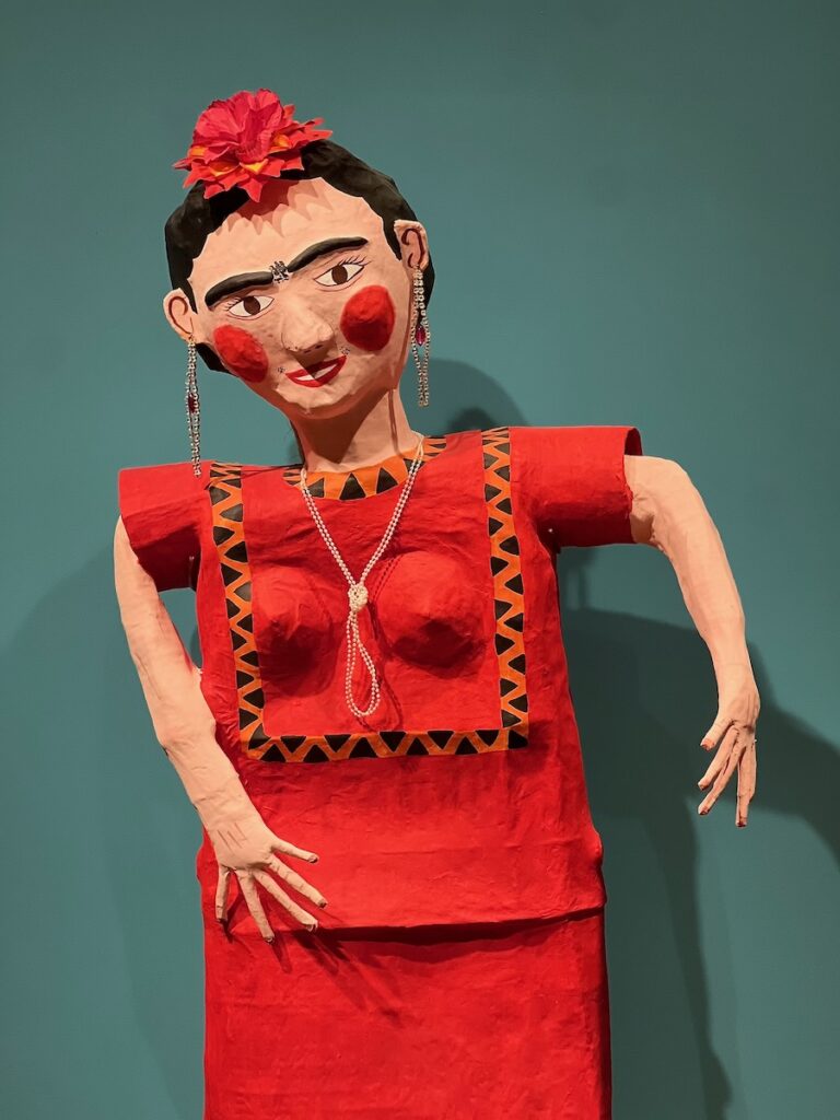 An art figure of Frida Khalo in a red dress and a red flower on her head.