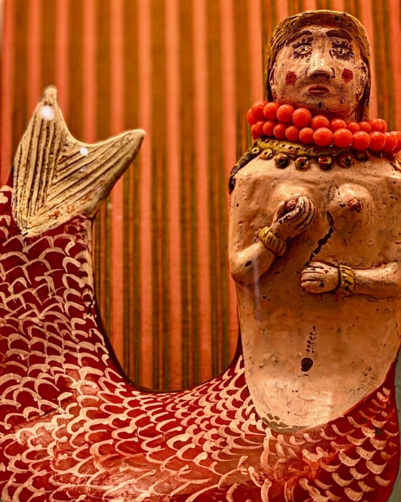 A wooden mermaid statue with a red tail and red bead necklace.