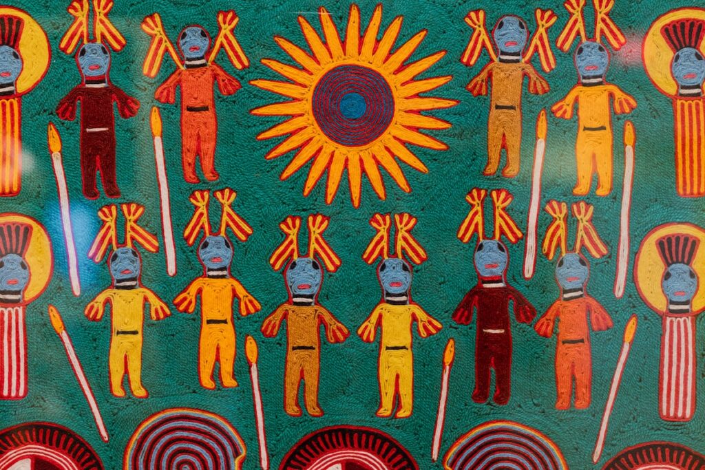 A vibrant colored piece of art make from yarn of figures around the sun.