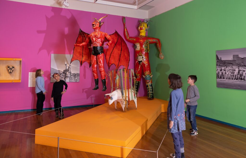 Children viewing an exhibit on a bright orange platform in a room with hot pink and vibrant green walls at the Santa Fe Museum of International Folk Art