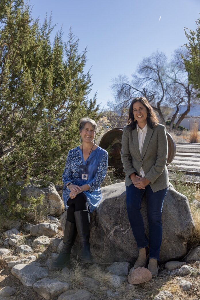 International Folk Art Market Behind the Scenes 2026 TABLE Magazine Two women from the International Folk Art Market lean against a rock outside in Santa Fe.