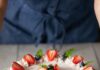 6 Recipes for a Red, White, and Blue 4th of July or Memorial Day A full gelatin cake in red, white, and blue colors decorated in strawberries, blueberries, and mint sits on a picnic like table.