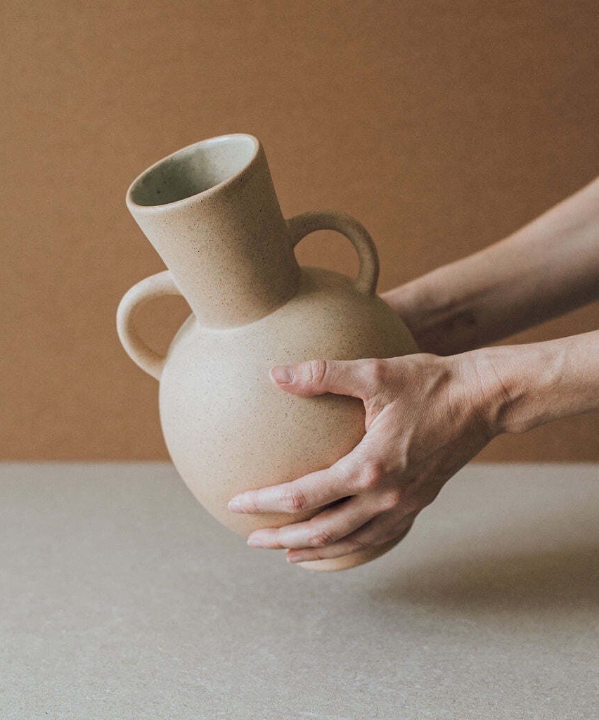 A person holds a clay vase in their hands.