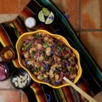 A yellow swiggly bowl with a Bean Salad inside beside little dishes of spices and limes.