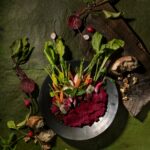 Beet muhammara dip topped with fresh carrots and radishes served with crusty bread and walnuts.