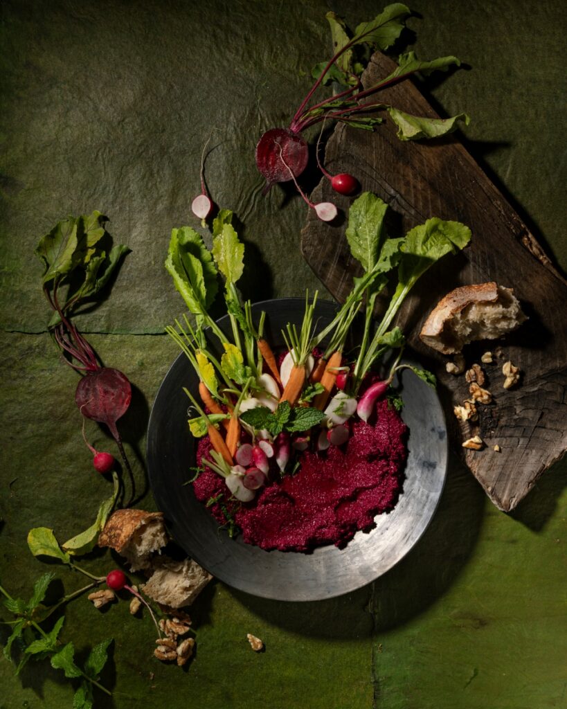 Beet muhammara dip topped with fresh carrots and radishes served with crusty bread and walnuts.