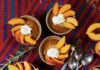 Butterscotch Budino (Italian Pudding) Small tins of Butterscotch Budino with whipped cream and slices of peaches on top, all on a red and blue cloth.