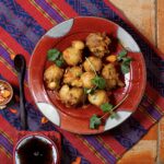 A red plate with white dots and Green Chile Hushpuppies on it and a red and purple cloth under the plate.