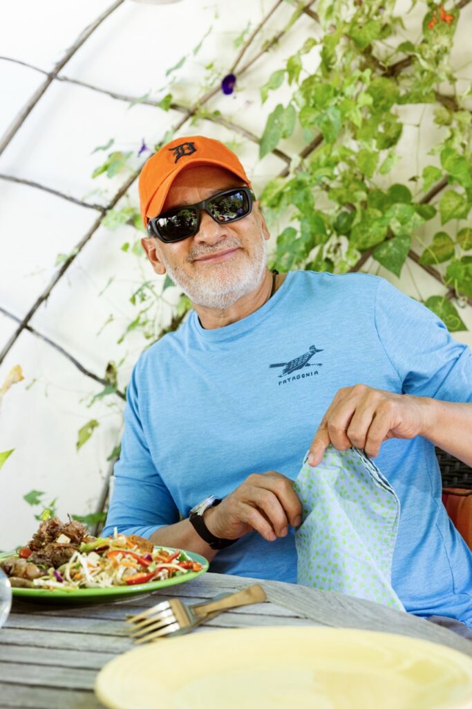 A man in an orange hat, sunglasses, and blue shirt beside a plate of food.