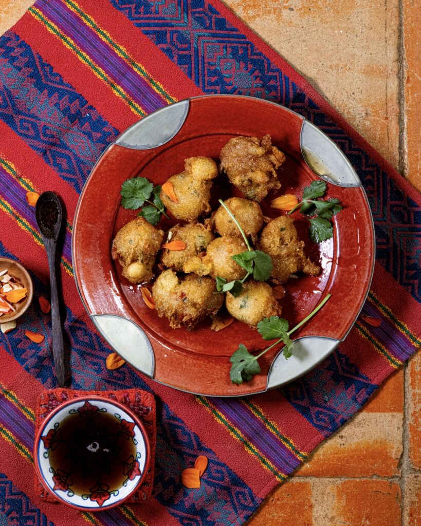 A red plate with white dots and Green Chile Hushpuppies on it and a red and purple cloth under the plate.