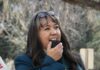 The Art of Generosity: How New Mexico Acequia Association is Protecting Vital Waterways A woman in a teal coat speaks into a megaphone microphone with glasses on top of her head.