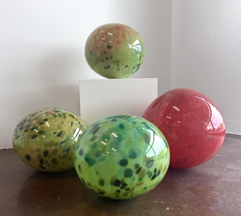 Four marble balls in a gallery space in green and pink colors.