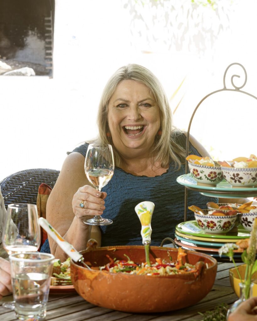 A woman at a dining table outside holding a wine glass in her hand.