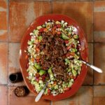 A red plate with a salad of veggies and shredded beef brisket on top.