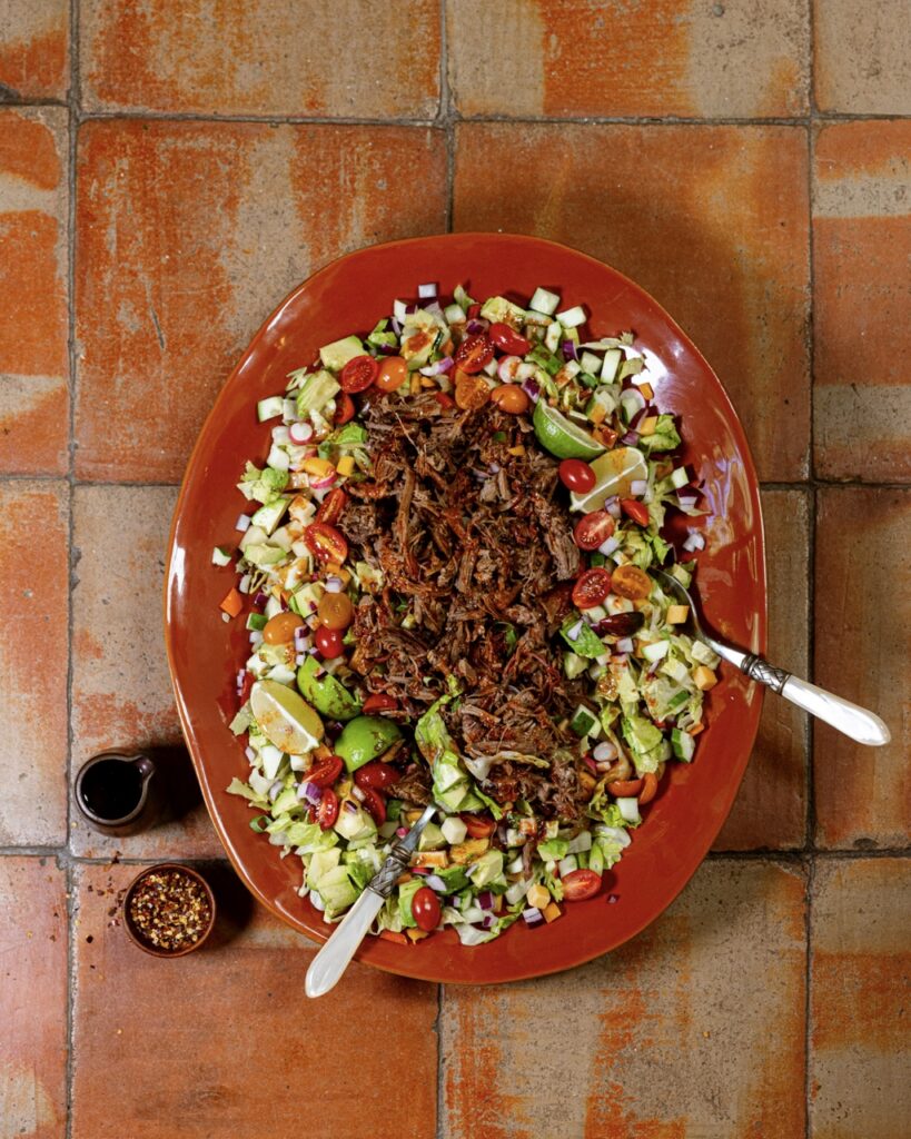 A red plate with a salad of veggies and shredded beef brisket on top.