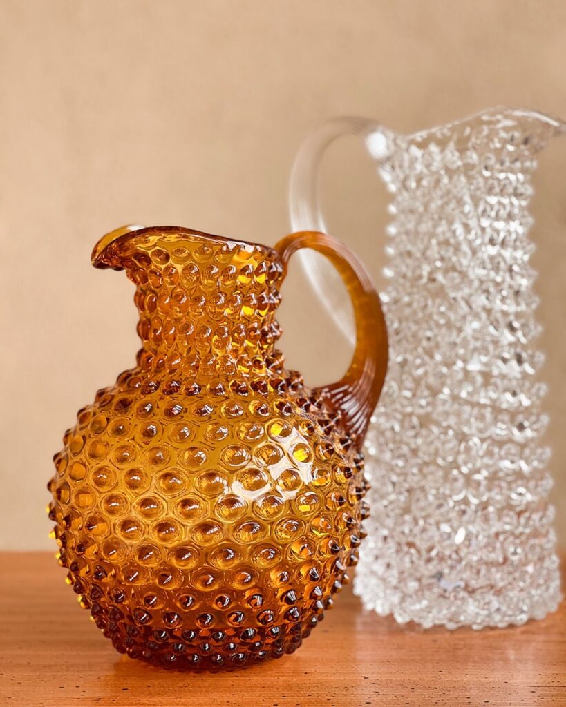 A spiky brown jug beside a clear spiky glass jug.