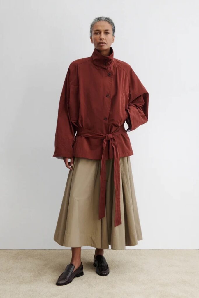 A woman in a long sleeve burnt orange top with a khaki skirt.